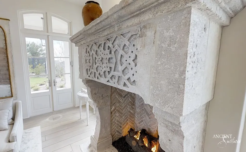 Intricately carved limestone fireplace mantel with a fretwork panel above a herringbone brick firebox