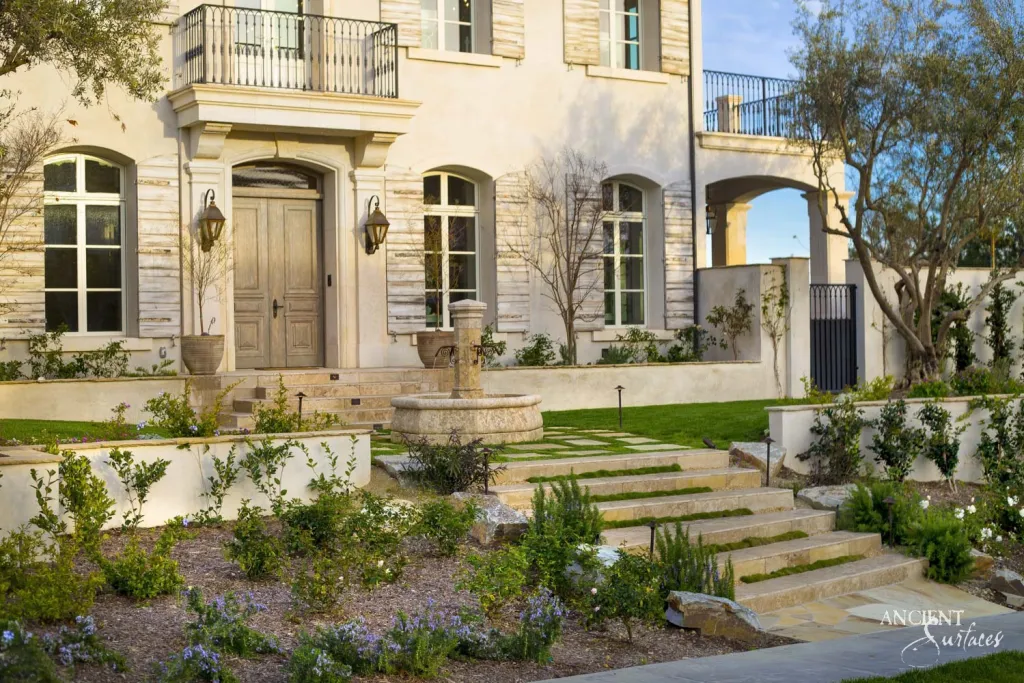 Provencal style villa entrance with a round carved stone fountain at the foot of a limestone paver stairway