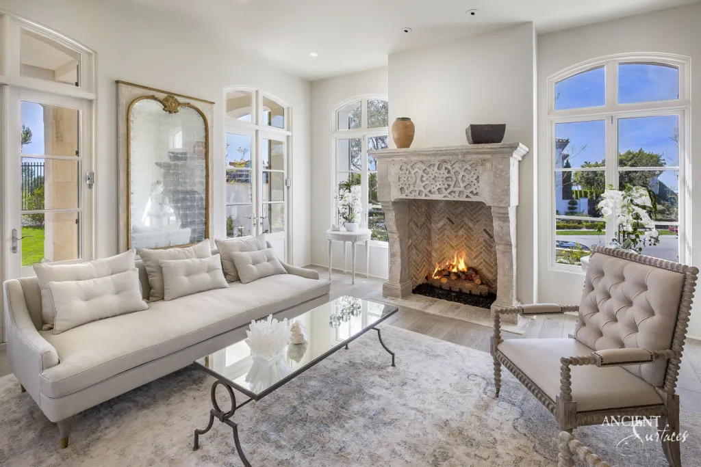 Carved limestone fireplace mantel anchoring a living room with French doors opening to the garden