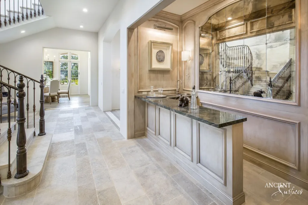 Limestone floor pavers leading past a butler's pantry with a dark stone counter near the staircase