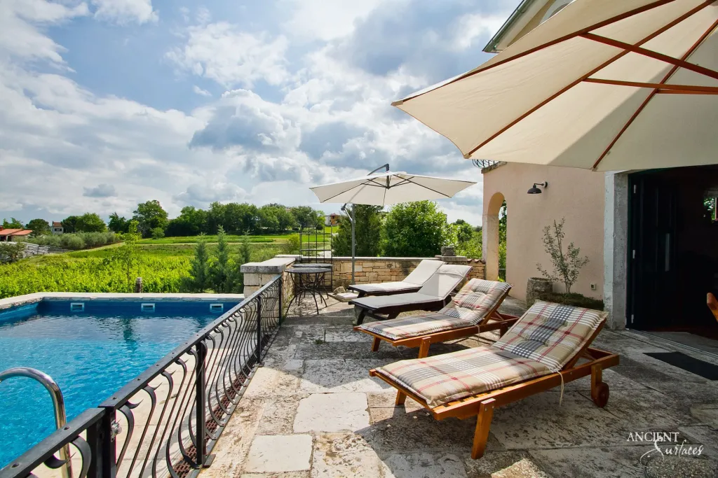 Reclaimed limestone pool terrace with wooden loungers overlooking vineyard covered hills