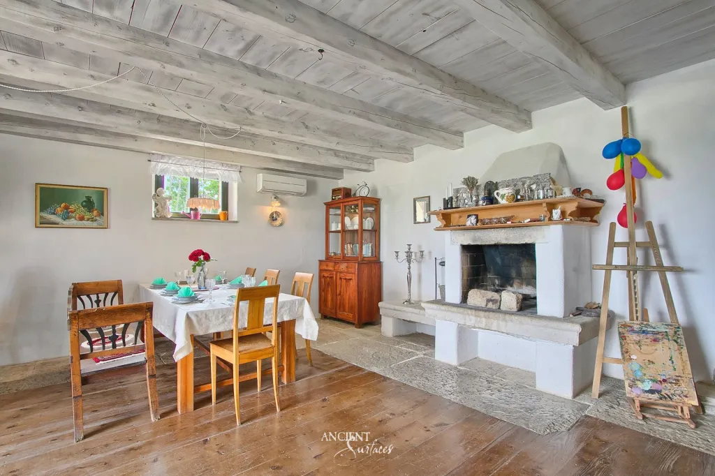 Rustic dining room with a plastered stone fireplace hearth beneath a wood beamed ceiling