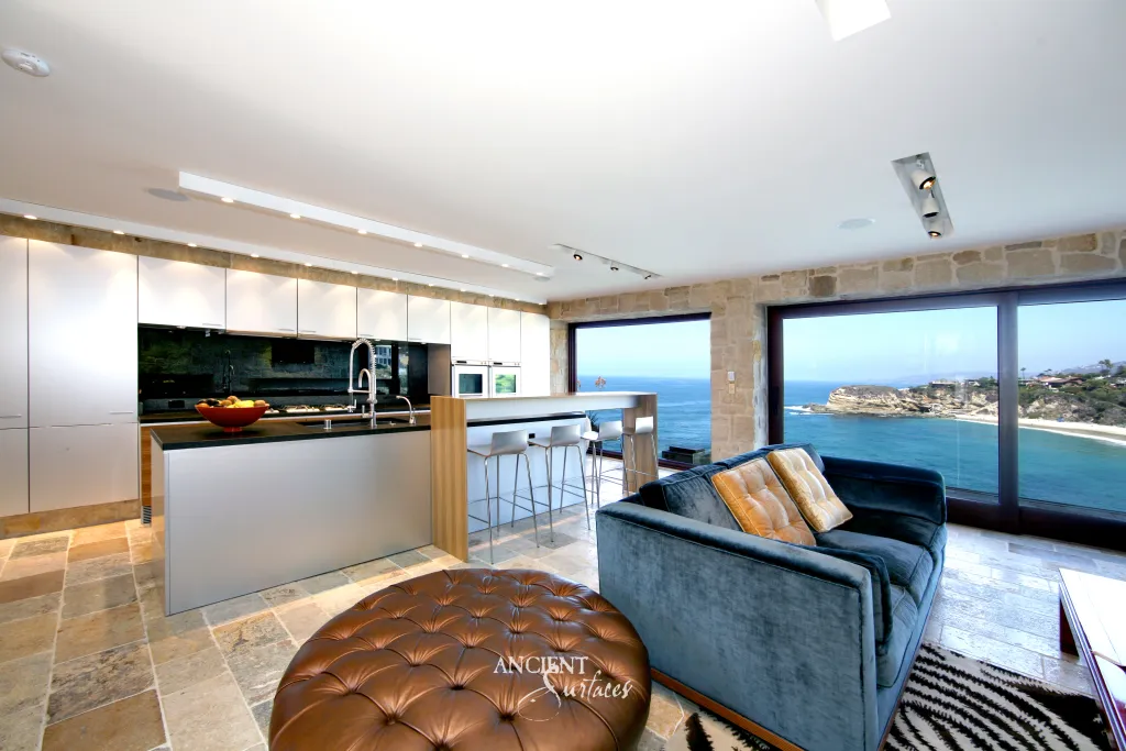 Open plan kitchen with limestone wall cladding and ocean view sliding doors overlooking a cliffside cove