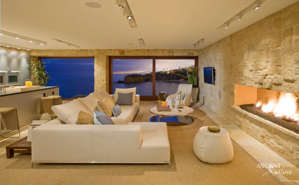 Linear fireplace built into a limestone clad wall in an oceanfront living room at dusk