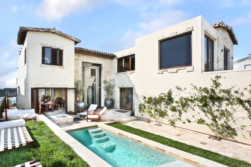 Rear elevation of a limestone clad villa with a stone coped swimming pool along the patio