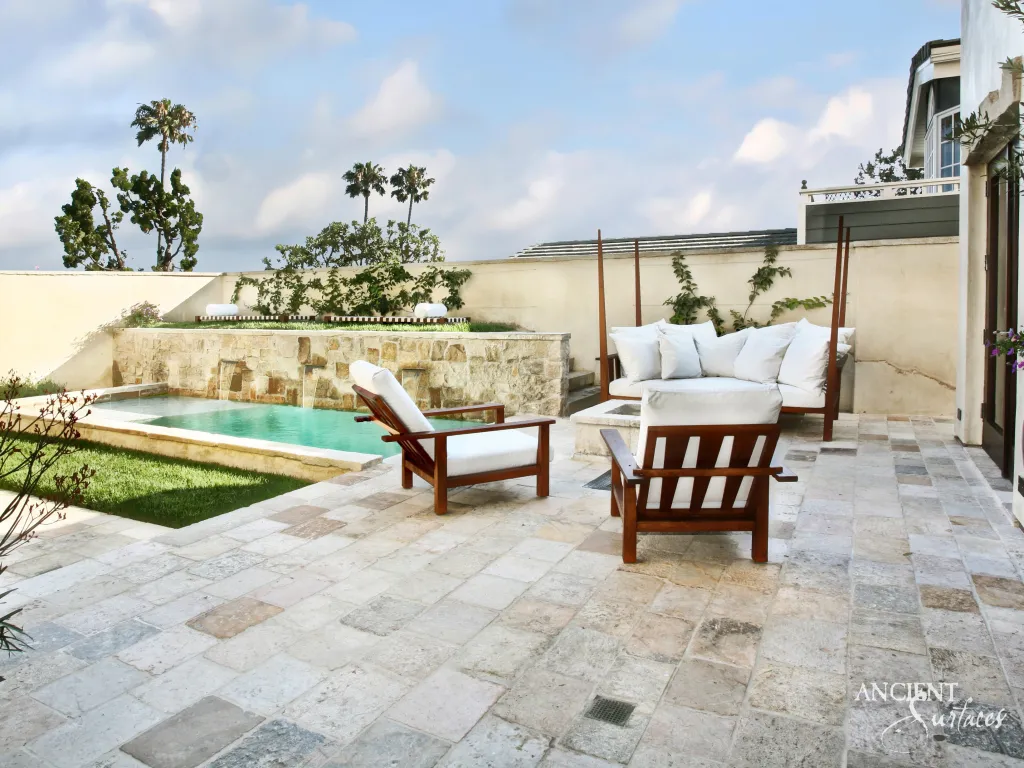 Large format limestone patio pavers surrounding a stone edged swimming pool and lounge chairs
