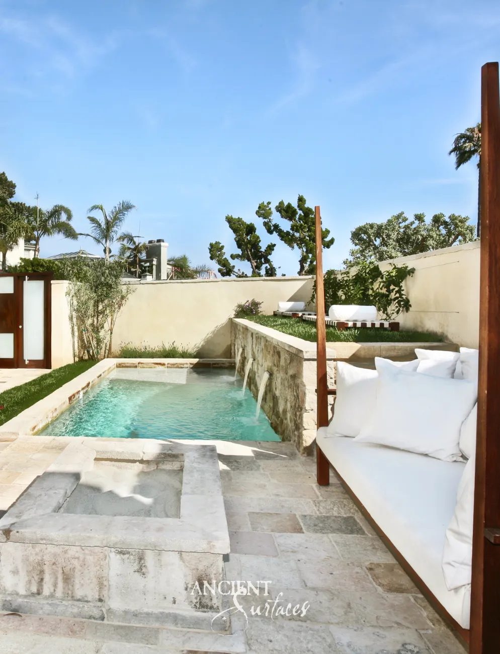 Stone wall with four carved spouts feeding a limestone coped swimming pool beside a stone clad fire pit
