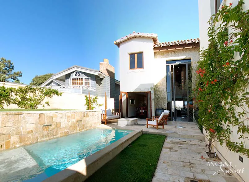 Limestone clad wall with a single water spout feeding a coped swimming pool beside the patio entrance
